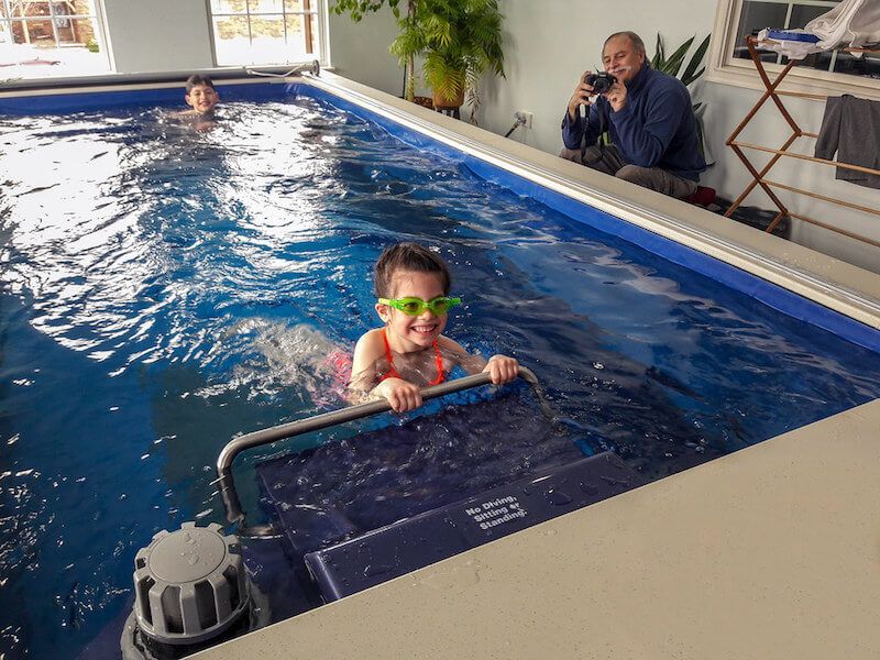 picture of a grandfather watches his grandkids swim and play in their sunroom Endless Pools installation