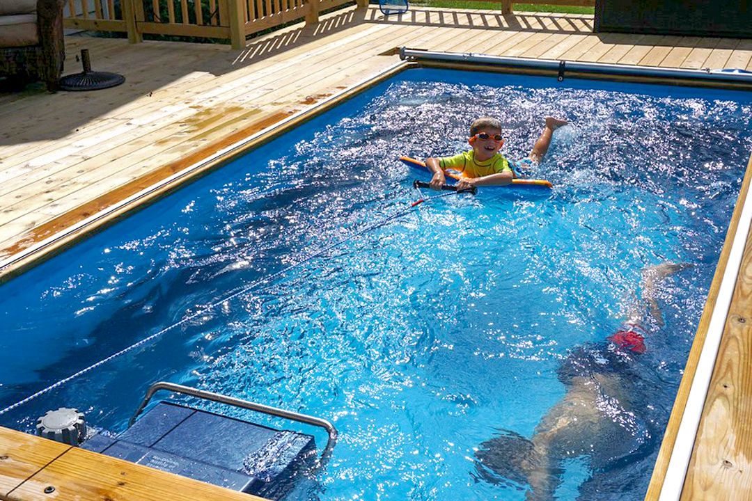 A picture of two boys swimming in a pool, one on a flotation device and the other underwater.