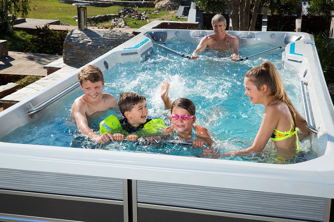 A picture of a man using a row kit at the back of a fitness spa while four children play at the front.