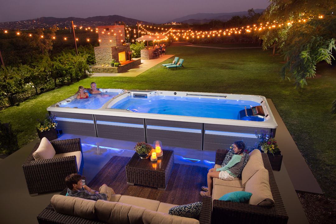 A picture of a man and a woman relaxing in one section of their swim spa while two children relax on the couches beside it.