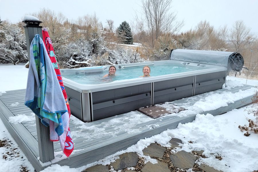 A picture of two children swimming in an outdoor pool surrounded by snow.